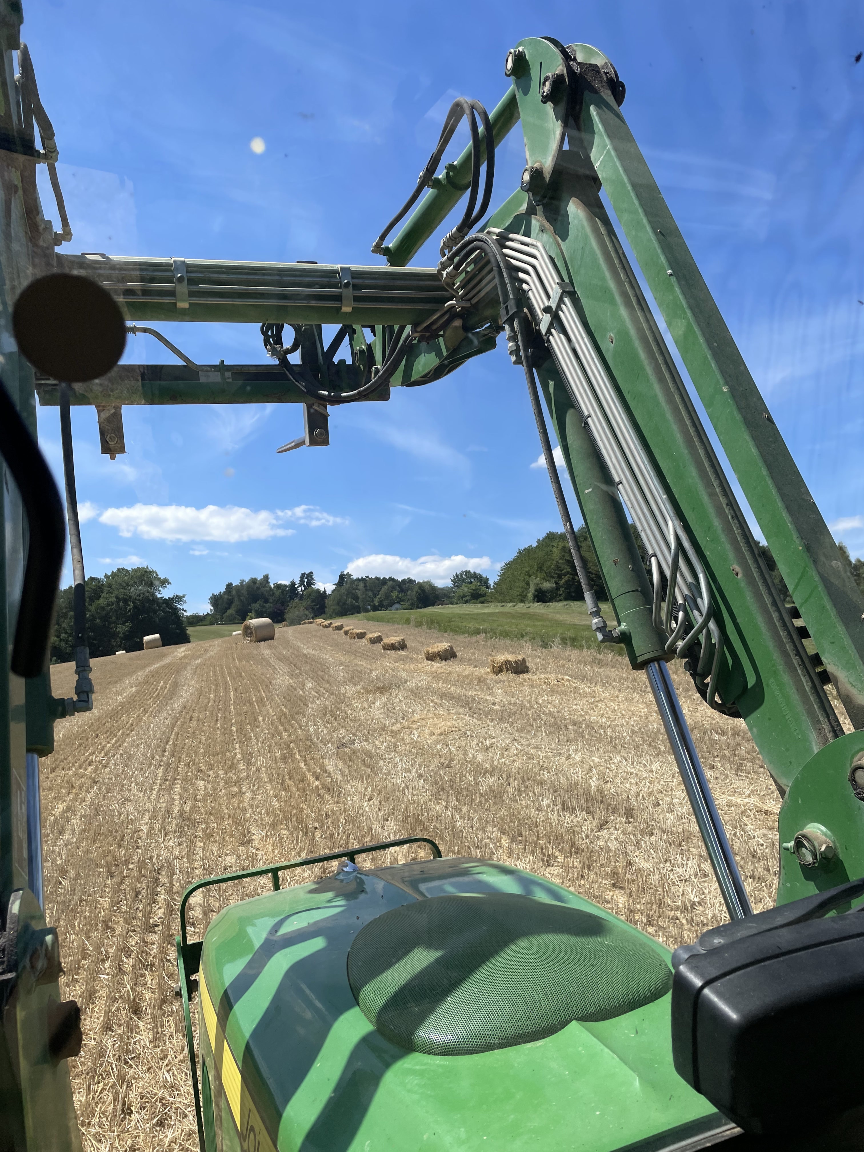Blick aus Traktor auf Strohballen auf Feld bei sonnigem Himmel auf Bio-Bauernhof in Niederbayern.